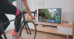 Asian woman cyclist is exercising in the house by cycling on trainer and play online bike games with TV