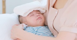 authentic shot of asian baby has fever and his mother checks temperature by thermometer on sofa in close up