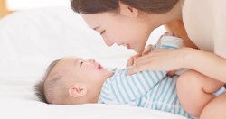 authentic shot of asian mother plays with her baby on the bed