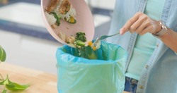 close up of asian woman scraping food leftovers or waste into kitchen bucket at home