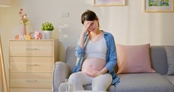 pregnancy feel depression - asian pregnant woman is suffering headache and abdominal pain sitting on sofa in the living room at home