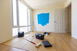 Empty room interior with a wooden floor and a half painted blue wall - A ladder and tins of paint