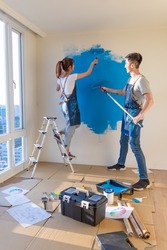 young asian couple decorate home - they painting wall with blue color together