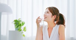side view of asian woman with brunette ponytail smile drinks a glass water happily in a white room