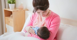authentic shot of asian mother sitting on bed is breastfeeding her baby