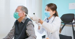 asian female doctor wearing face mask is using tuning fork for hearing tests to elder senior man patient in hospital