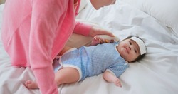 authentic shot of asian baby has fever and his mother checks body temperature by thermometer on bed