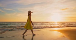 side view of asian woman wearing beautiful yellow dress walking by beach at golden sunset - Female tourist on summer vacation