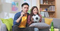 asian couple watching soccer game together with joy and excitement the man is holing a remote control 