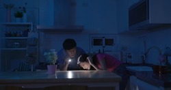 asian couple using flashlight to illuminate are looking for something after power outage in kitchen at home