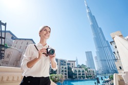 Enjoying travel in United Arabian Emirates. Happy young woman with camera taking photo in Dubai Downtown.