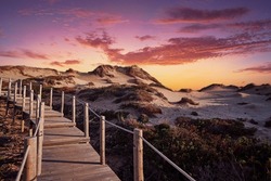 Wooden pedestrian walkway through Sintra-Cascais natural park with beautiful sunset sky. Wild sandy landscape, with part of Cresmina Dunes. Beautiful scenery in Portugal.