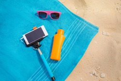 Vacation, technology and protection. Must have accessories on the sea beach. Smartphone, selfie stick, sunscreen and sunglasses. Top view.