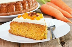 Piece of carrot cake with icing decorated dried apricots and walnut on white plate on rustic table