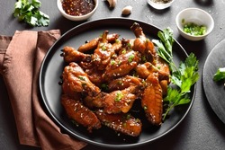 Sticky honey-soy chicken wings on plate over dark stone background. Close up view