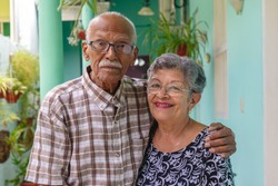 An smiling elderly couple, both wearing glasses.
