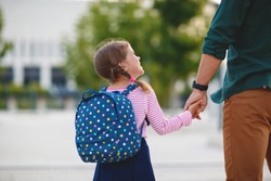 first day at school. father leads a little child school girl in first grade