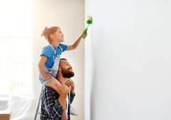 Repair in the apartment. Happy family father and child daughter  paints the wall with yellow paint