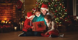 Merry Christmas! happy family mother father and children with magic gift near tree at evening at home