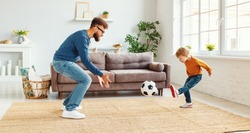Bearded man in glasses  catching ball while teaching boy to play football in cozy room at home