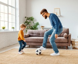 Full length cheerful boy laughing   near bearded father with ball while playing football at home together