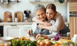 Happy family cheerful young woman embracing mature mother while preparing healthy dish with fresh vegetables in home kitchen