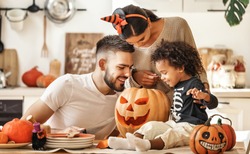 Cheerful multi ethnic family parents with son smiling  while creating jack o lantern from pumpkin during Halloween celebration in kitchen at home