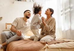 happy family multiethnic mother, father and son  laughing, playing,and jumping in bed in bedroom at home