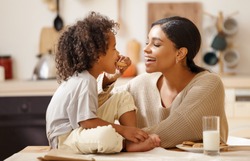 happy african american family: mother and little son eat cookies with milk for breakfast at home