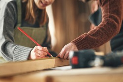 Crop unrecognizable craftswoman making marks on wooden detail while working with anonymous colleague in carpentry workshop