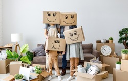 concept of moving to a new apartment and a mortgage. Unrecognizable couple and kids wearing carton boxes on heads standing together in new flat with various stuff during relocation