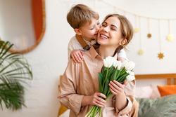 tender son kisses the happy mother and gives her a bouquet of tulips, congratulating her on mother's day during holiday celebration at home