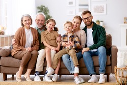 Big happy family. Portrait of grandparents, mother, father and two their cute kids, sister and brother, sitting together on coach at home and smiling at camera. Mortgage loan and real estate concept