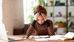 Stressed young afro american woman holding head in hands and feeling demotivated while sitting at her home office and working remotely on laptop. Depressed female student tired of onling learning