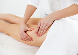 Beauty treatments for weight lost. Cropped shot of therapist or masseur doing lymphatic drainage or anti cellulite massage on legs for woman client lying at spa center. Body care concept