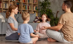 Young parents meditating with kids at home. beautiful family father, mother and two kids with closed eyes practicing yoga while sitting in circle in lotus pose