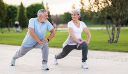 Energize your morning. Full length of active happy elderly family couple in sportswear working out together in city park in morning. Joyful senior husband and wife making sport outdoors, warming up
