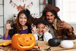 Joyful happy african american family parents and little boy son in Halloween costumes making scary gesture at camera while making jack o lantern