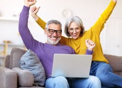 Overjoyed excited senior family couple celebrating success while sitting on sofa with laptop, happy retired man and woman receiving email with positive good news, seniors winning lottery