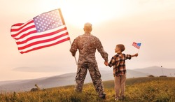 Rear view of military man father holding   son's hand   with american flag   and enjoying amazing summer nature view on sunny day, happy male soldier dad reunited with son after US army
