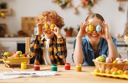 Happy mother and little son   holding painted colorful Easter eggs in front of eyes while decorating them with food dyes in cozy kitchen at home. Easter craft activities for families