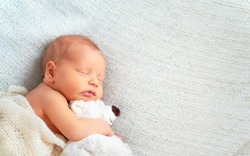 Cute newborn baby sleeps with a toy teddy bear white