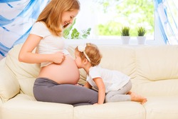 happy family. Pregnant mother and baby daughter kissing relaxing and playing on the sofa at home