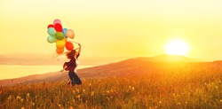 Happy cheerful girl with balloons running across meadow at sunset on nature in summer