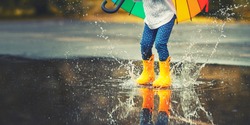 Feet of child in yellow rubber boots jumping over a puddle in the rain