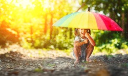 Happy child girl laughs and plays under the summer rain with an umbrella