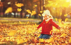 happy child girl throws autumn leaves and laughs outdoors