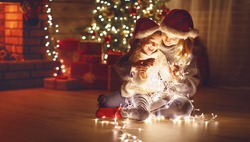 Merry Christmas! mother and child daughter with a glowing Christmas garland near tree