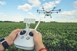 Controlling a remote Octocopter drone. Drone flight remote controller in man hands. Agriculture drone flies over the green field.