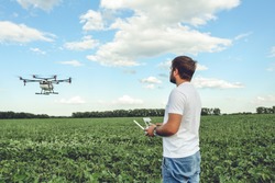 Young man operating of flying drone octocopter at the green field. Professional agriculture drone flying with blue sky.